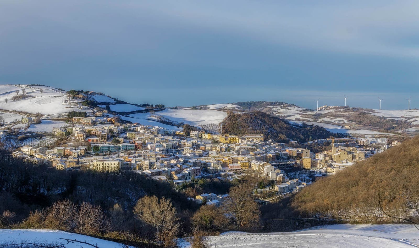 Bonefro sotto la neve sulla collina, con le pale eoliche all'orizzonte