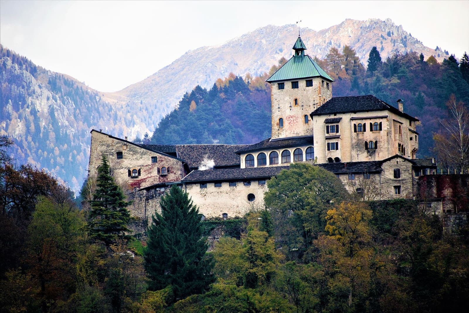 Castel Ivano visto da ovest, sul colle tra i boschi, con le montagne sullo sfondo