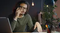 Persona al telefono alla scrivania mentre lavora al laptop