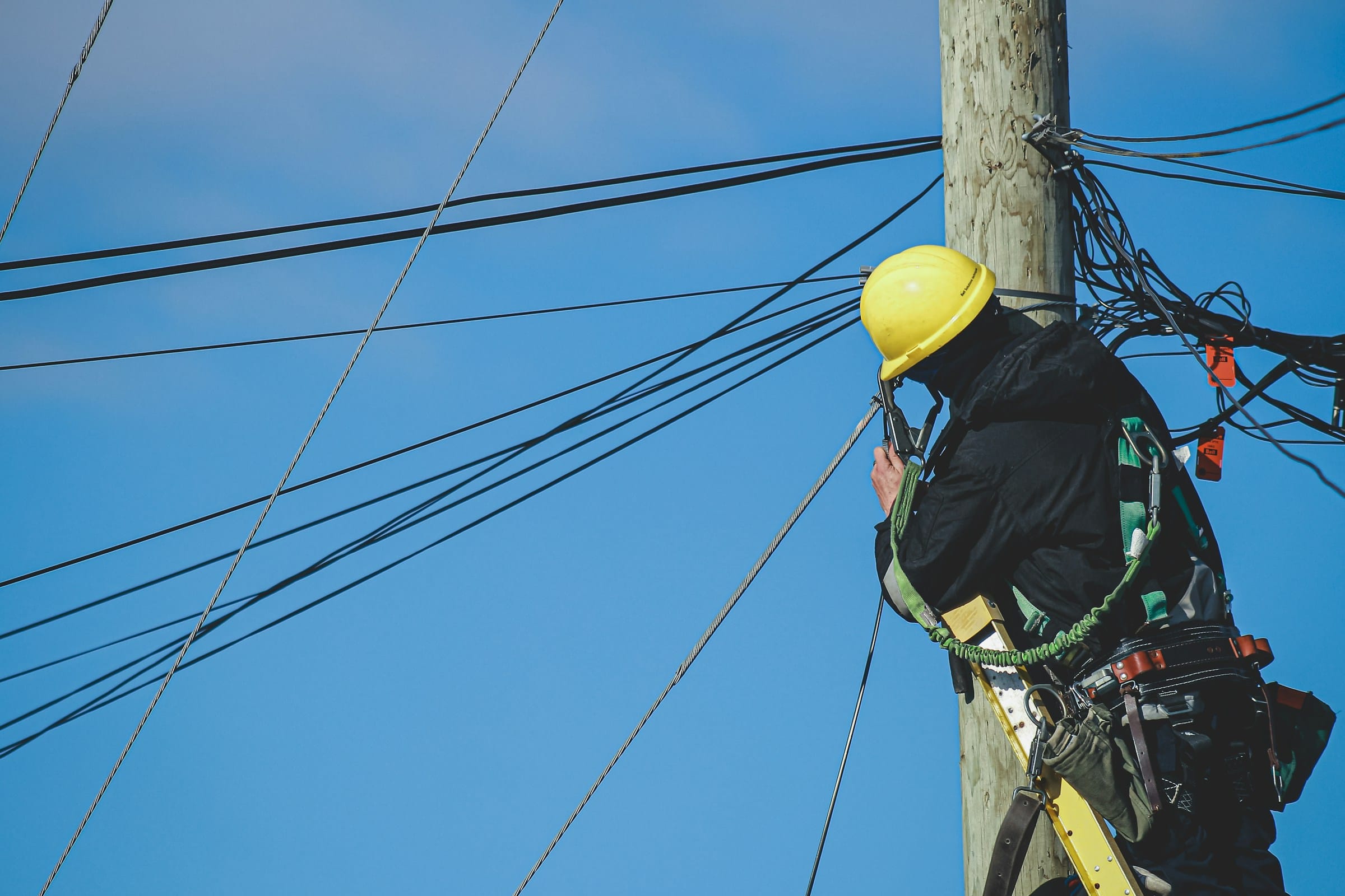 Tecnico con casco e imbracatura al lavoro su un palo con cavi di rete