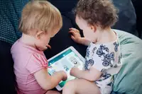 Bambini piccoli sul divano che usano insieme un tablet