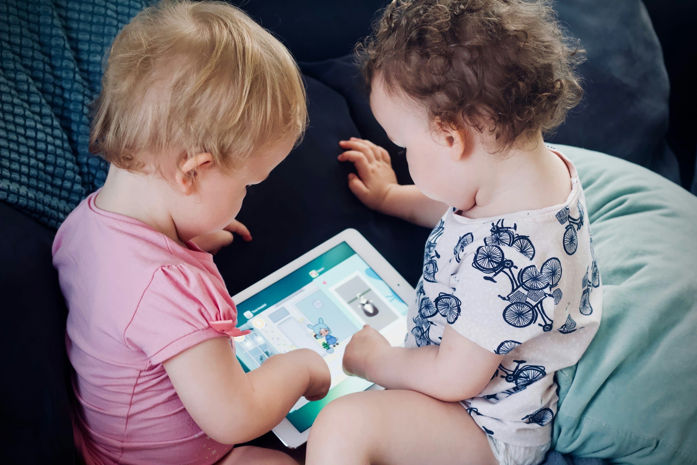 Bambini piccoli sul divano che usano insieme un tablet