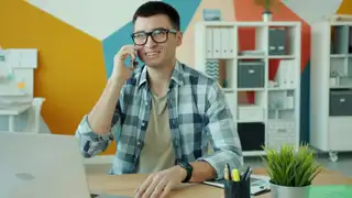 Operatore sorridente al telefono mentre segue un cliente dalla scrivania